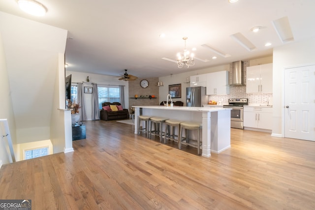 kitchen with wall chimney exhaust hood, white cabinetry, hanging light fixtures, stainless steel appliances, and light hardwood / wood-style floors