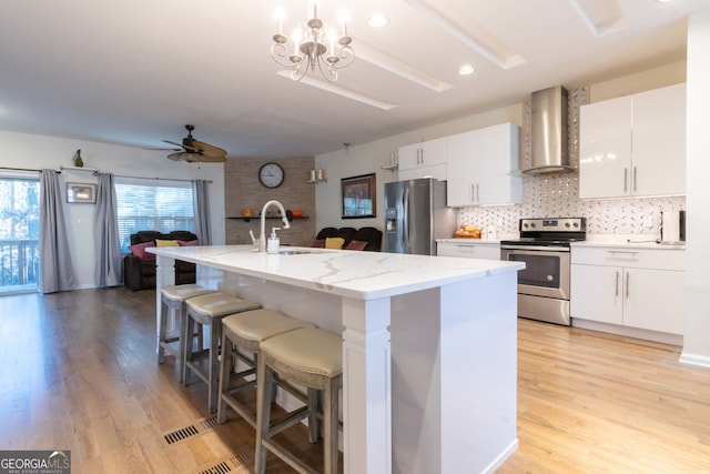 kitchen with stainless steel appliances, white cabinetry, wall chimney range hood, and an island with sink