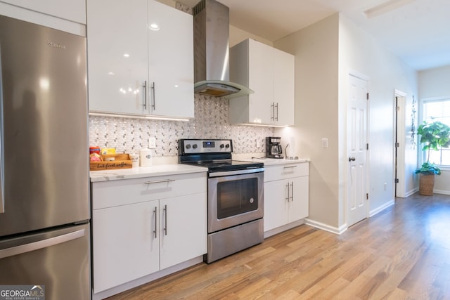 kitchen with wall chimney range hood, light hardwood / wood-style flooring, backsplash, stainless steel appliances, and white cabinets