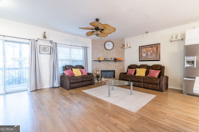 living room featuring a stone fireplace, light hardwood / wood-style flooring, and ceiling fan