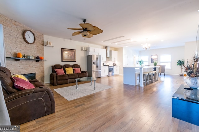 living room featuring a stone fireplace, light hardwood / wood-style flooring, and ceiling fan with notable chandelier