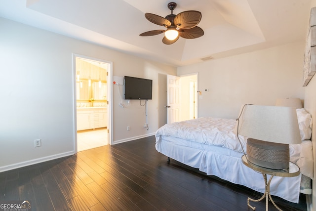 bedroom featuring visible vents, baseboards, wood finished floors, ensuite bath, and a raised ceiling