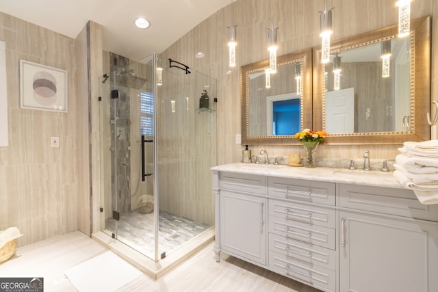 full bath with a sink, tile walls, double vanity, and a shower stall