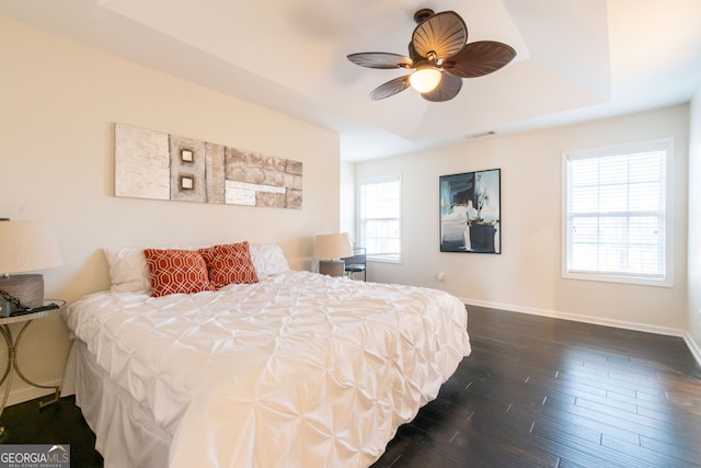 bedroom with dark wood-type flooring, ceiling fan, and a tray ceiling