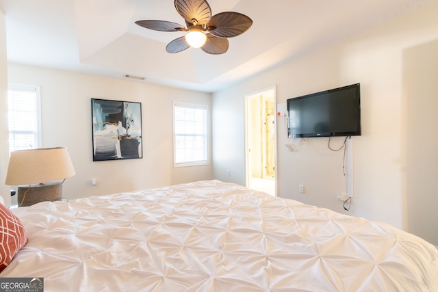 bedroom featuring ceiling fan, ensuite bath, and a tray ceiling