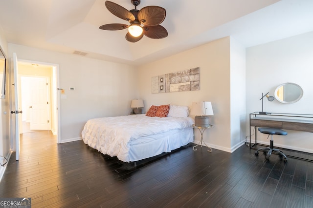 bedroom with dark hardwood / wood-style floors, ceiling fan, and a tray ceiling