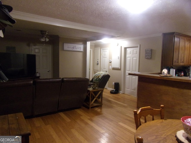 living room featuring ceiling fan, ornamental molding, light hardwood / wood-style floors, and a textured ceiling