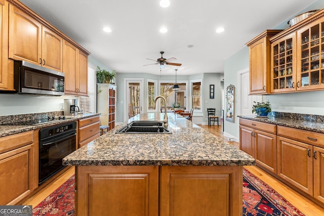 kitchen with light hardwood / wood-style flooring, sink, a center island with sink, and black appliances