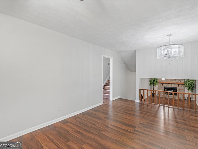 unfurnished living room featuring a fireplace, a textured ceiling, dark wood-type flooring, and a chandelier