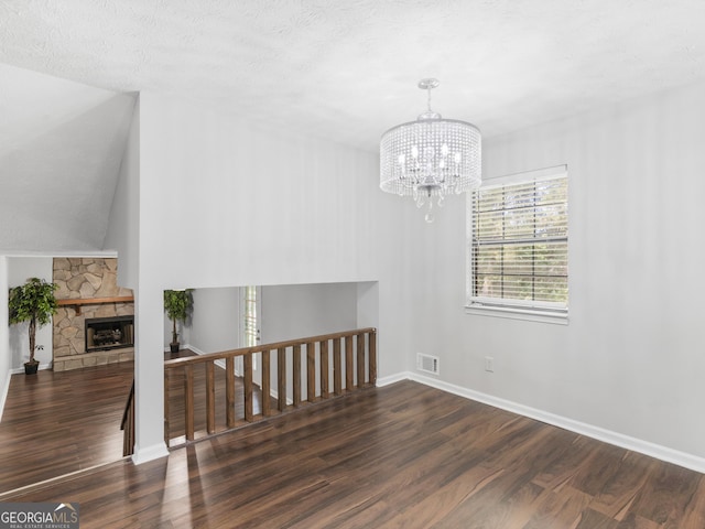 empty room with lofted ceiling, dark hardwood / wood-style floors, an inviting chandelier, and a fireplace