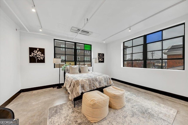 bedroom with concrete flooring, rail lighting, and multiple windows