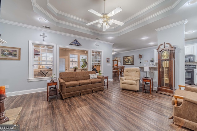 living room with crown molding, a tray ceiling, dark wood-type flooring, and ceiling fan