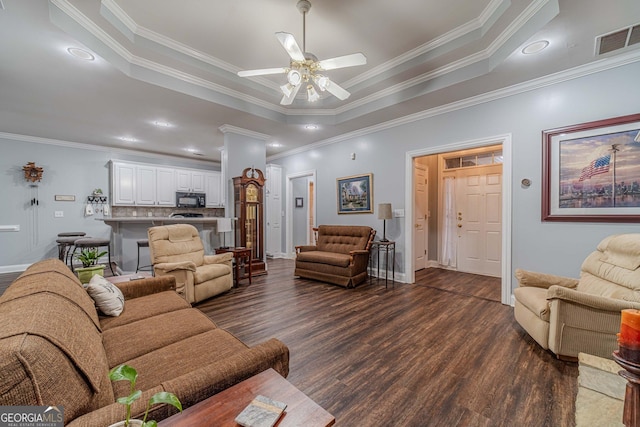 living room featuring crown molding, dark wood-type flooring, a raised ceiling, and ceiling fan