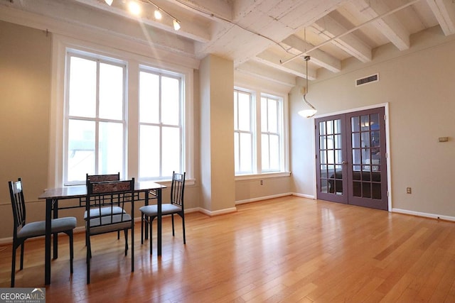 dining room with beam ceiling, light wood-type flooring, and french doors