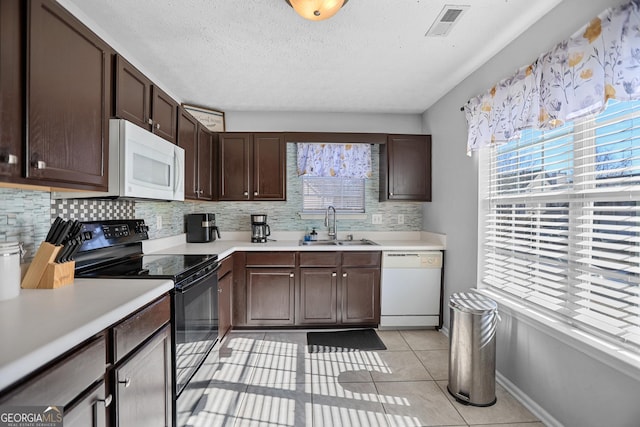 kitchen with dark brown cabinetry, sink, light tile patterned floors, and white appliances