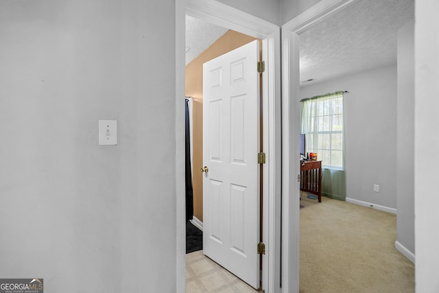 hallway featuring light colored carpet and a textured ceiling