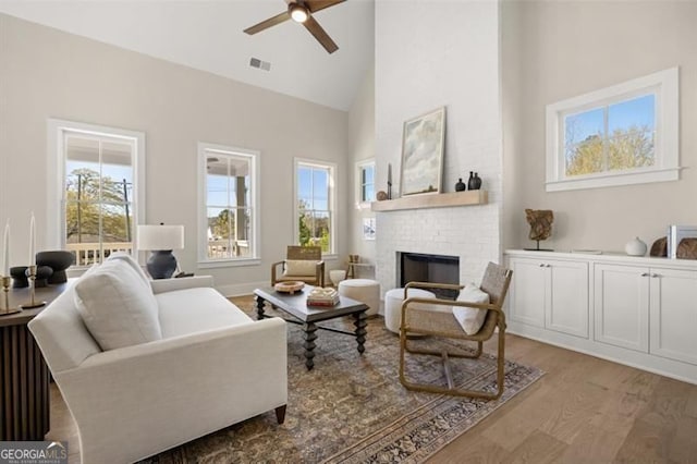 sitting room featuring light wood finished floors, visible vents, a ceiling fan, a fireplace, and high vaulted ceiling