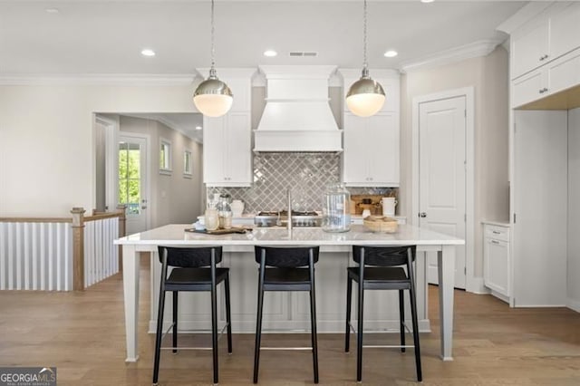 kitchen featuring an island with sink, light wood finished floors, premium range hood, and white cabinetry