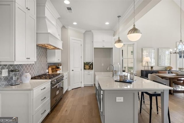 kitchen with visible vents, white cabinetry, wood finished floors, premium range hood, and high end range