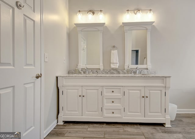 bathroom with double vanity, baseboards, wood finished floors, and a sink