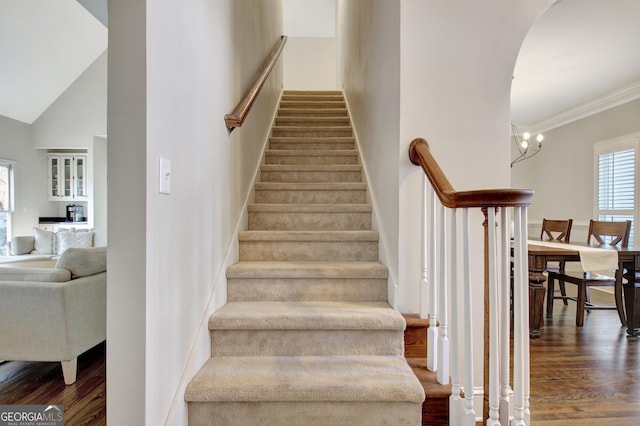stairway with a towering ceiling, baseboards, wood finished floors, and crown molding