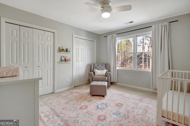 bedroom featuring carpet flooring, baseboards, visible vents, a ceiling fan, and two closets