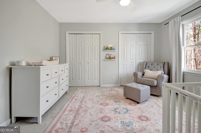 bedroom featuring ceiling fan, two closets, baseboards, and light carpet