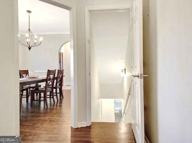 hall featuring wood finished floors, arched walkways, a notable chandelier, and ornamental molding