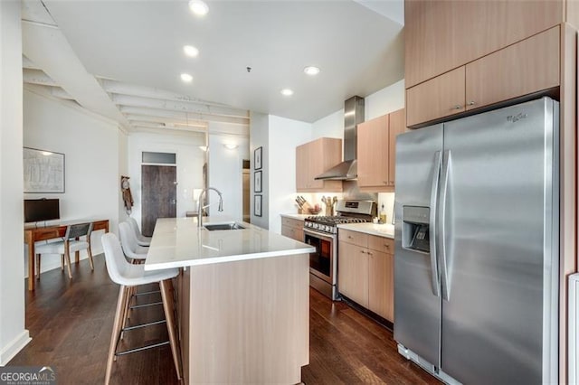 kitchen featuring dark wood-type flooring, wall chimney exhaust hood, sink, an island with sink, and stainless steel appliances