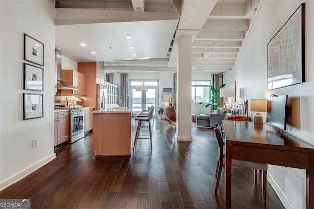 kitchen with a kitchen island, appliances with stainless steel finishes, decorative columns, dark wood-type flooring, and wall chimney range hood