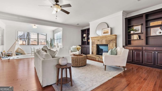 living room with a stone fireplace, dark wood-type flooring, ornamental molding, and ceiling fan