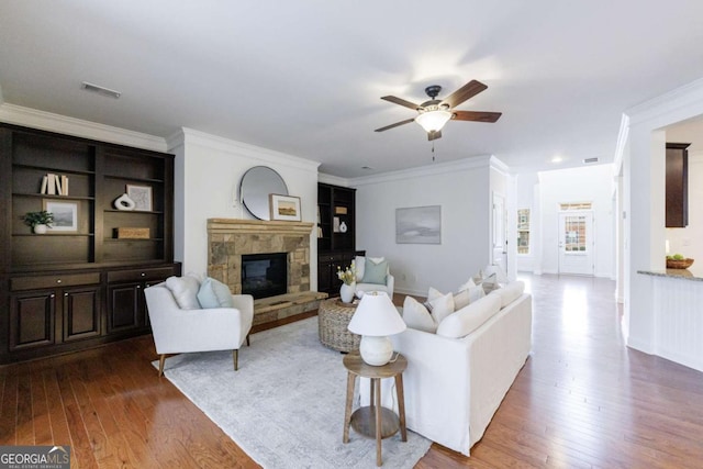 living room with wood-type flooring, ornamental molding, ceiling fan, and a fireplace