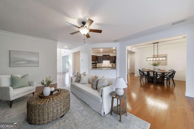 living room featuring crown molding, ceiling fan, and light wood-type flooring