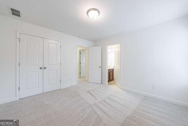 unfurnished bedroom featuring connected bathroom, light colored carpet, and a closet