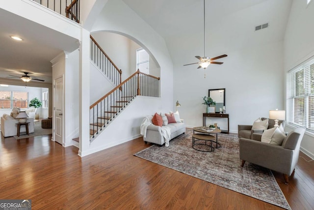 living room featuring dark wood-type flooring, ceiling fan, and a towering ceiling