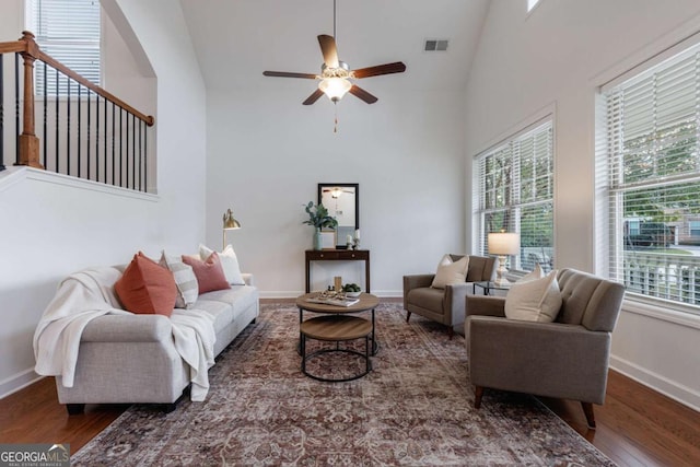 living room with ceiling fan, a towering ceiling, wood-type flooring, and plenty of natural light