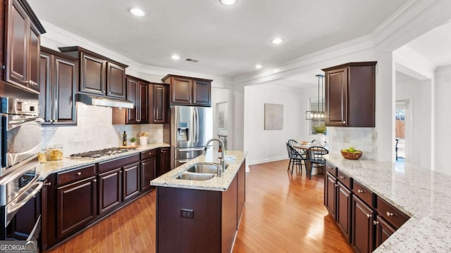 kitchen featuring light stone counters, an island with sink, stainless steel appliances, and sink