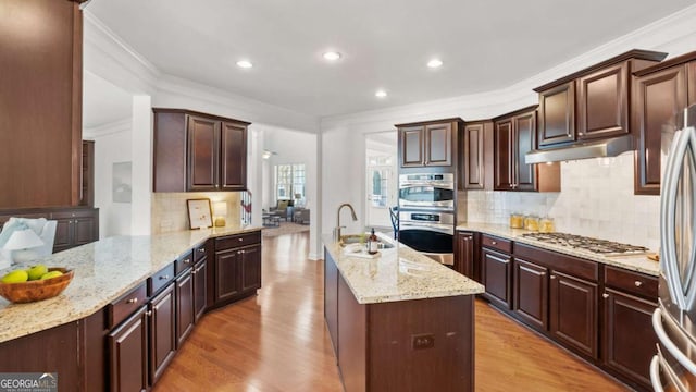 kitchen featuring appliances with stainless steel finishes, light stone countertops, sink, and light wood-type flooring