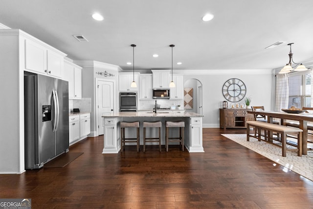 kitchen with appliances with stainless steel finishes, hanging light fixtures, light stone countertops, an island with sink, and white cabinets