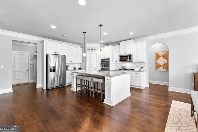 kitchen featuring appliances with stainless steel finishes, decorative light fixtures, a center island with sink, and white cabinets