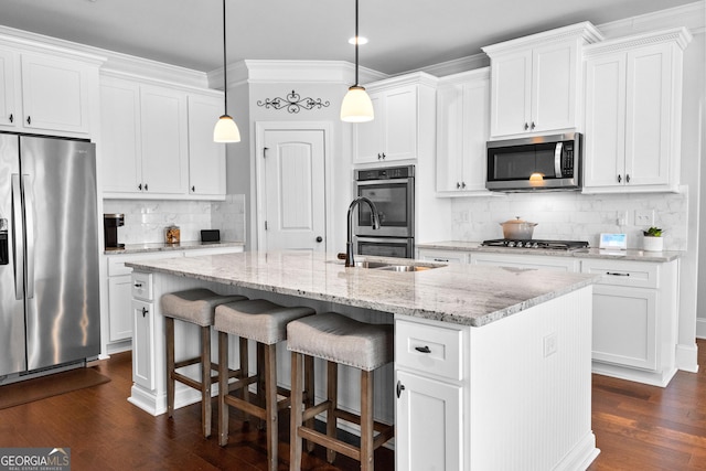 kitchen featuring appliances with stainless steel finishes, white cabinets, hanging light fixtures, light stone countertops, and a center island with sink