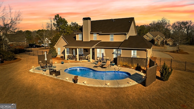 pool at dusk with a lawn and a patio area