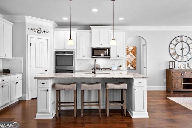 kitchen featuring stainless steel appliances, light stone countertops, a center island with sink, and decorative light fixtures