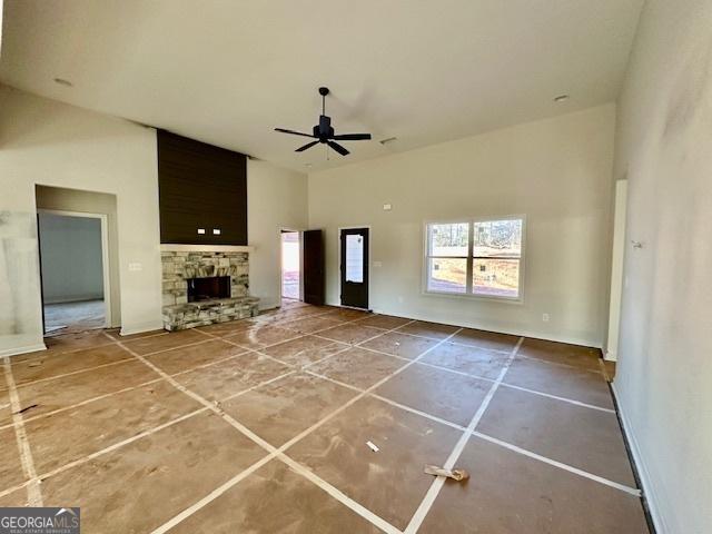 unfurnished living room featuring a stone fireplace, ceiling fan, and a high ceiling