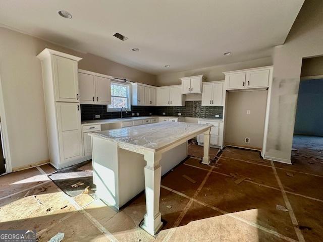 kitchen featuring a breakfast bar, sink, a kitchen island, white cabinets, and backsplash