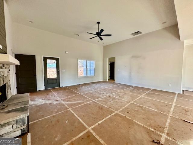 unfurnished living room featuring a high ceiling, a stone fireplace, and ceiling fan