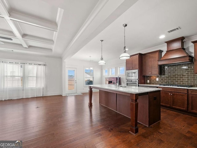kitchen featuring a breakfast bar, an island with sink, backsplash, custom exhaust hood, and stainless steel appliances