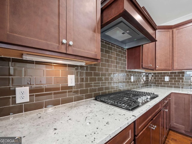 kitchen featuring decorative backsplash, light stone countertops, stainless steel gas cooktop, and custom exhaust hood