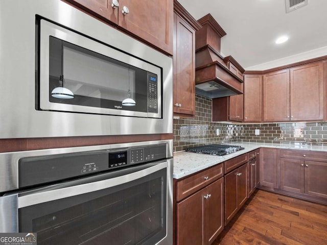kitchen with appliances with stainless steel finishes, dark hardwood / wood-style floors, light stone countertops, and backsplash