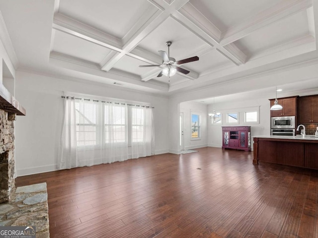 living room featuring a stone fireplace, ceiling fan with notable chandelier, dark hardwood / wood-style flooring, coffered ceiling, and beam ceiling